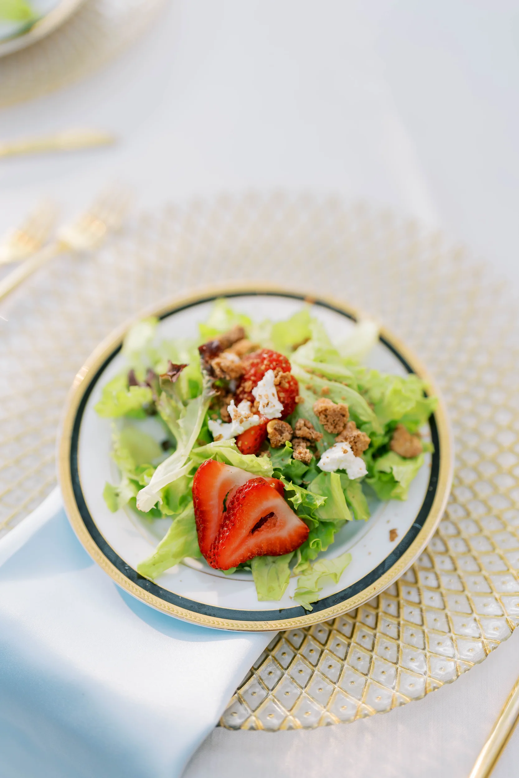 a small salad with strawberries on a white plate with a gold rim