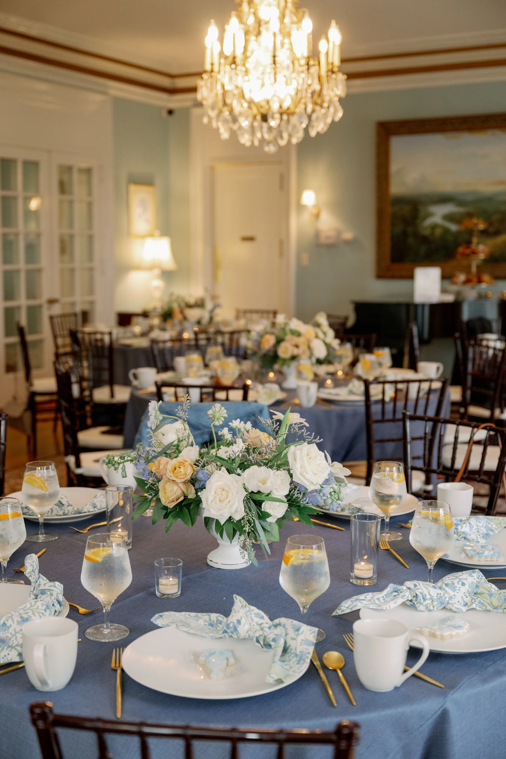 A dining room with a blue tablecloth, white plates, and gold utensils.