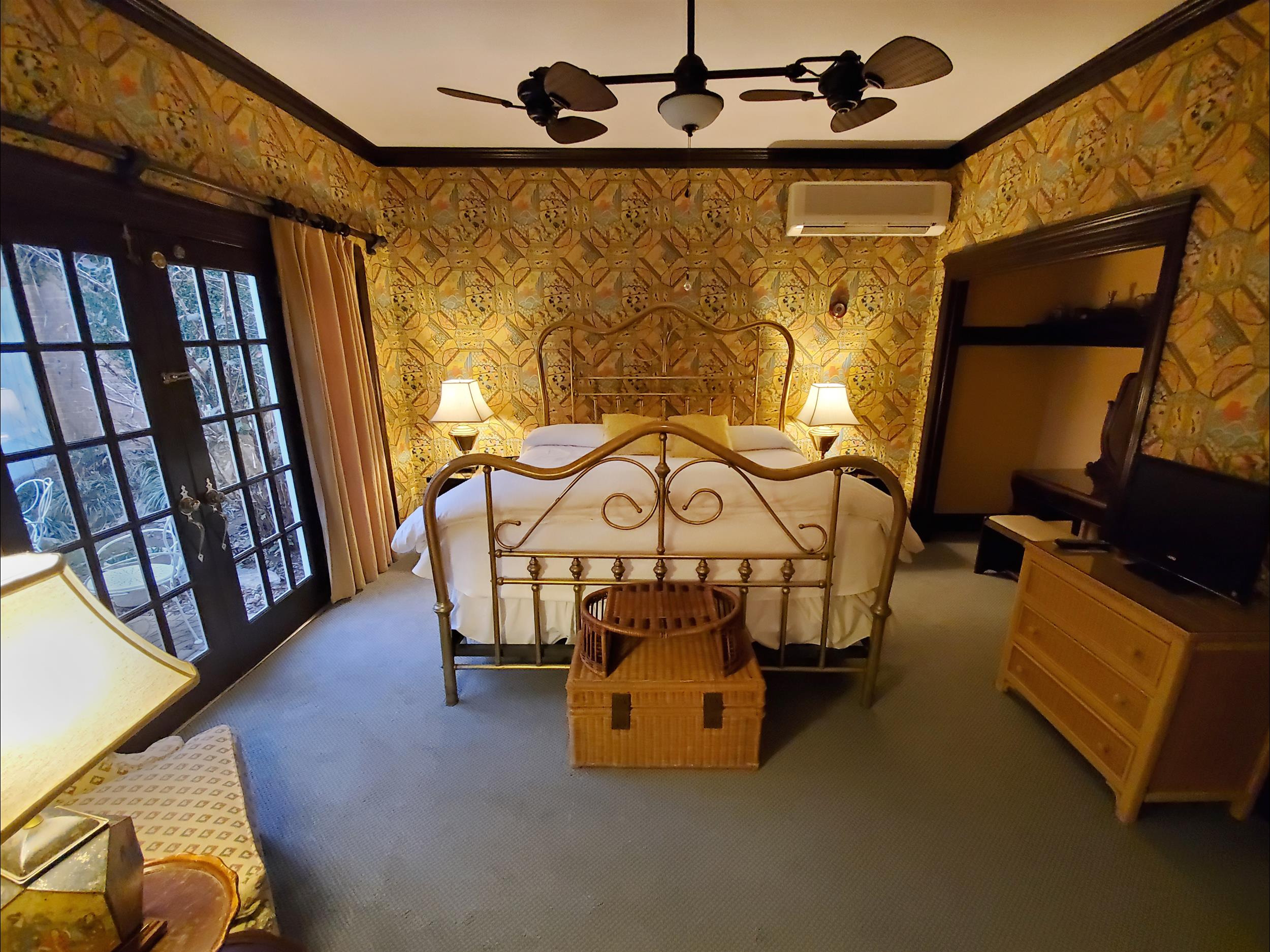A wide-angle view of a bedroom with a large bed, patterned wallpaper, and a ceiling fan.