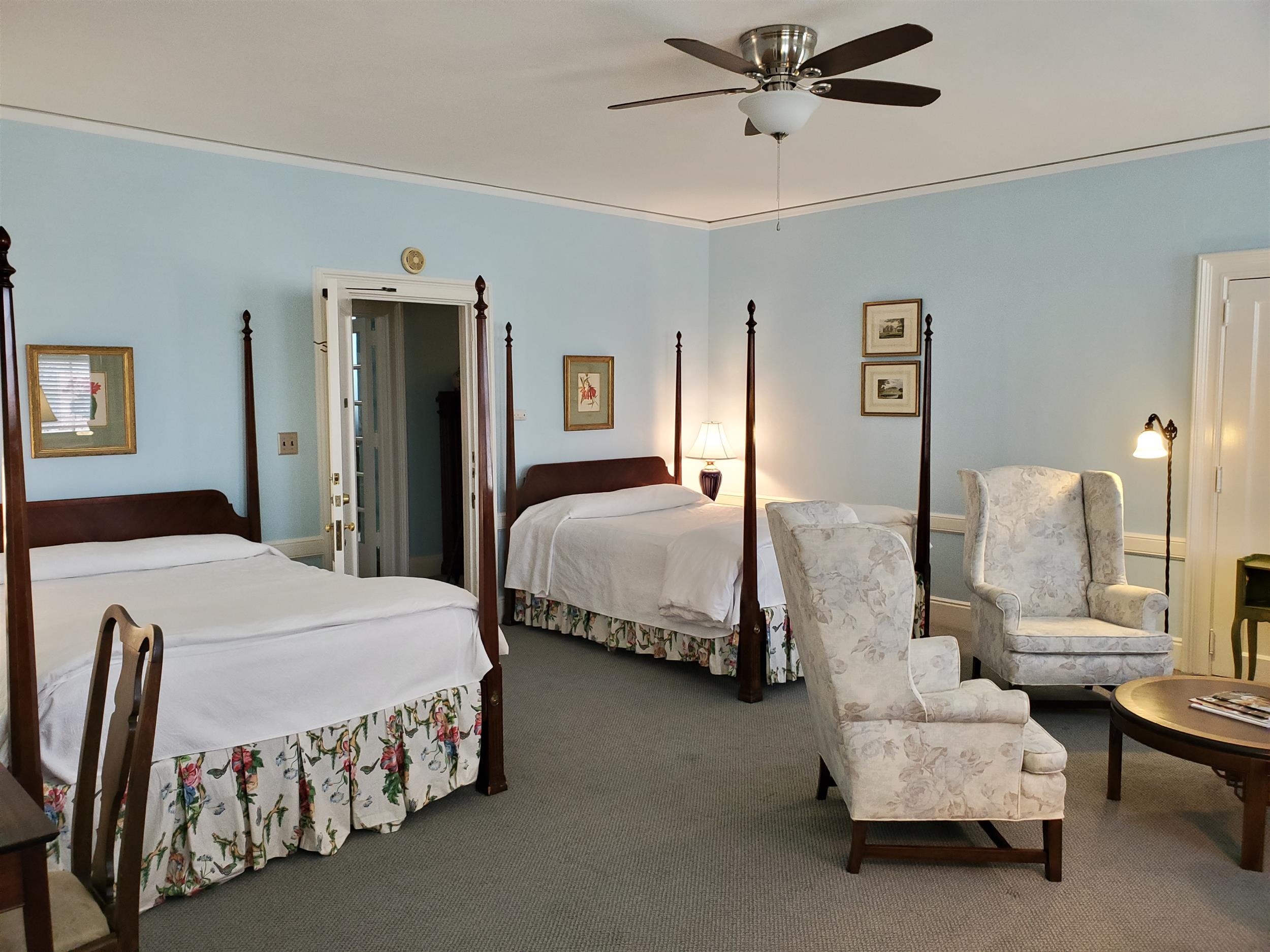 A hotel room with two beds, two chairs, and a table.